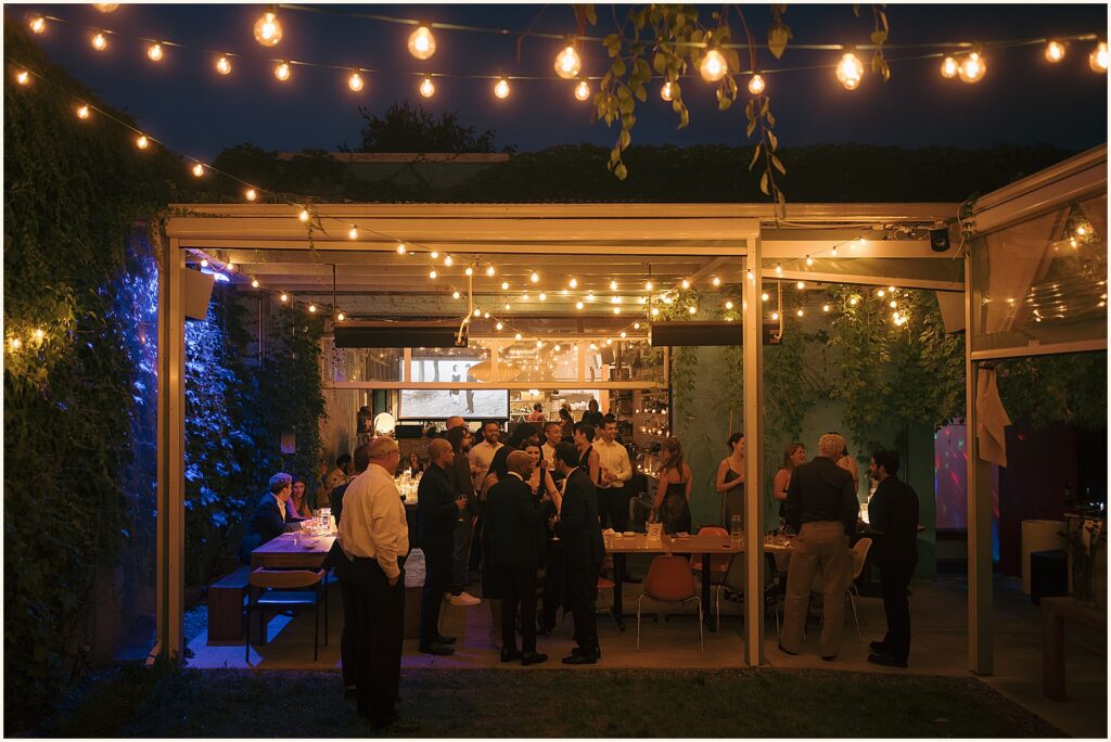 Wedding guests sit on a patio lit by strings of lights at a Portland wedding.