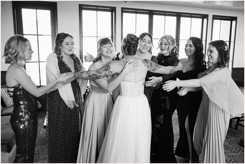 A group of bridesmaids reach towards a bride for a group hug.