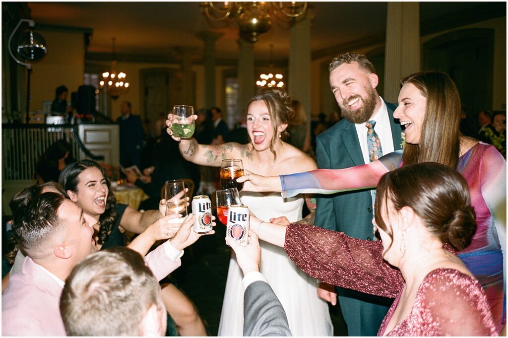 A bride and groom cheers with wedding guests.