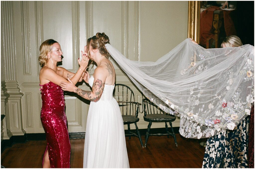 Bridesmaids help a bride put on her veil before a wedding ceremony at Colony House Newport.