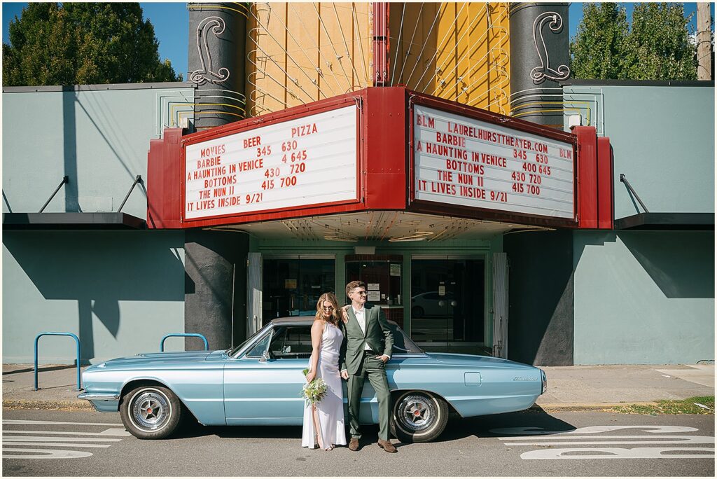 A bride and groom pose in front of a classic car parked in front of a theater at their Portland elopement.