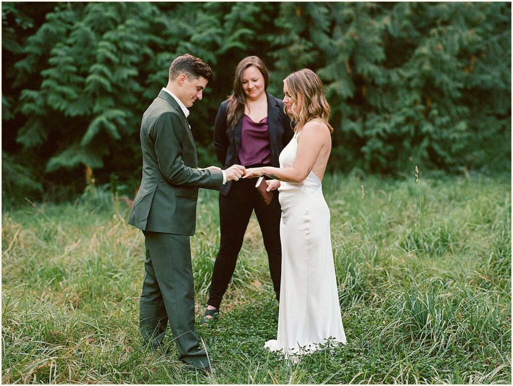 A groom puts a ring on a bride's finger at a Portland elopement in a park.