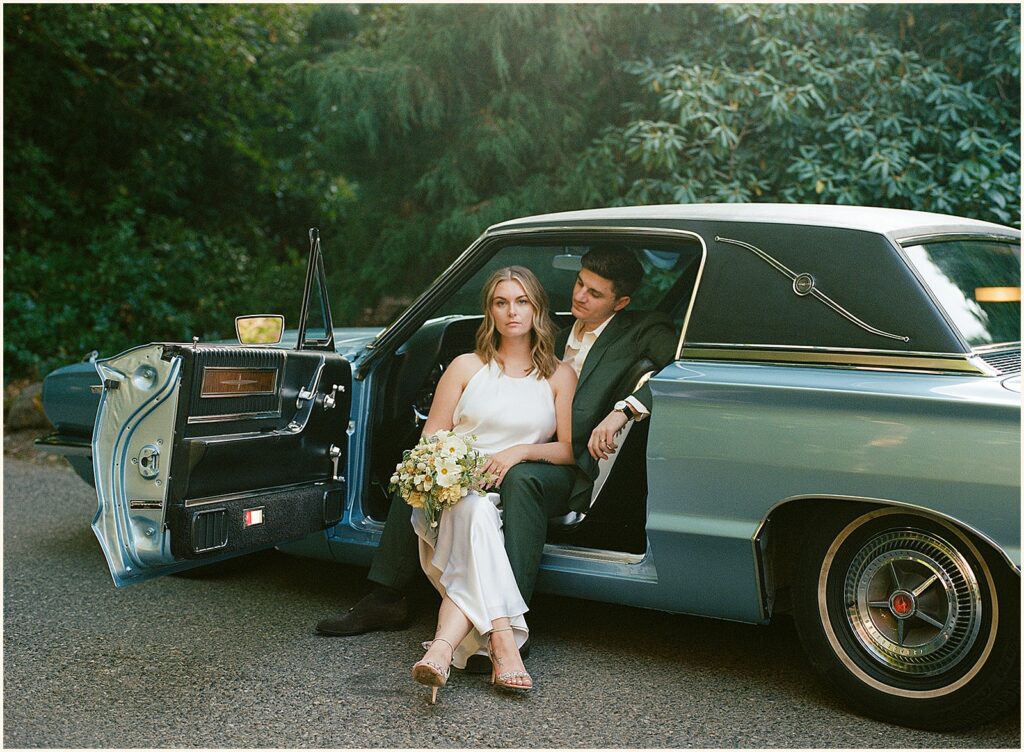 A bride and groom pose in a classic car in a Portland park.