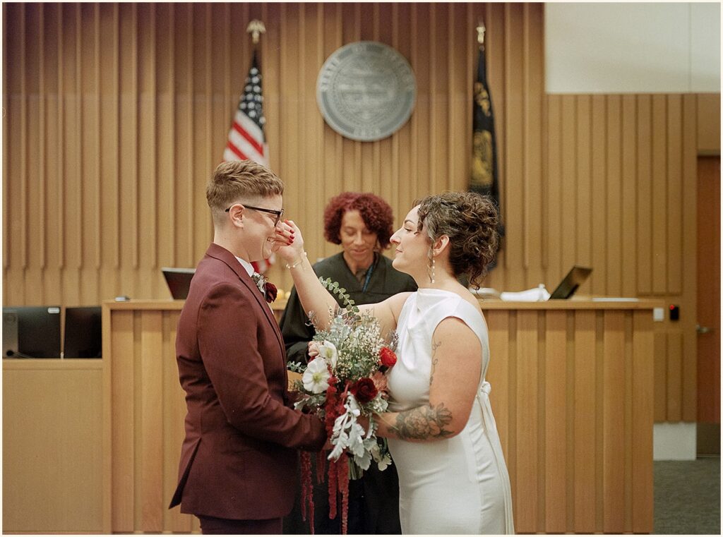 A bride wipes a tear from her spouse's face at a courthouse elopement in Portland.
