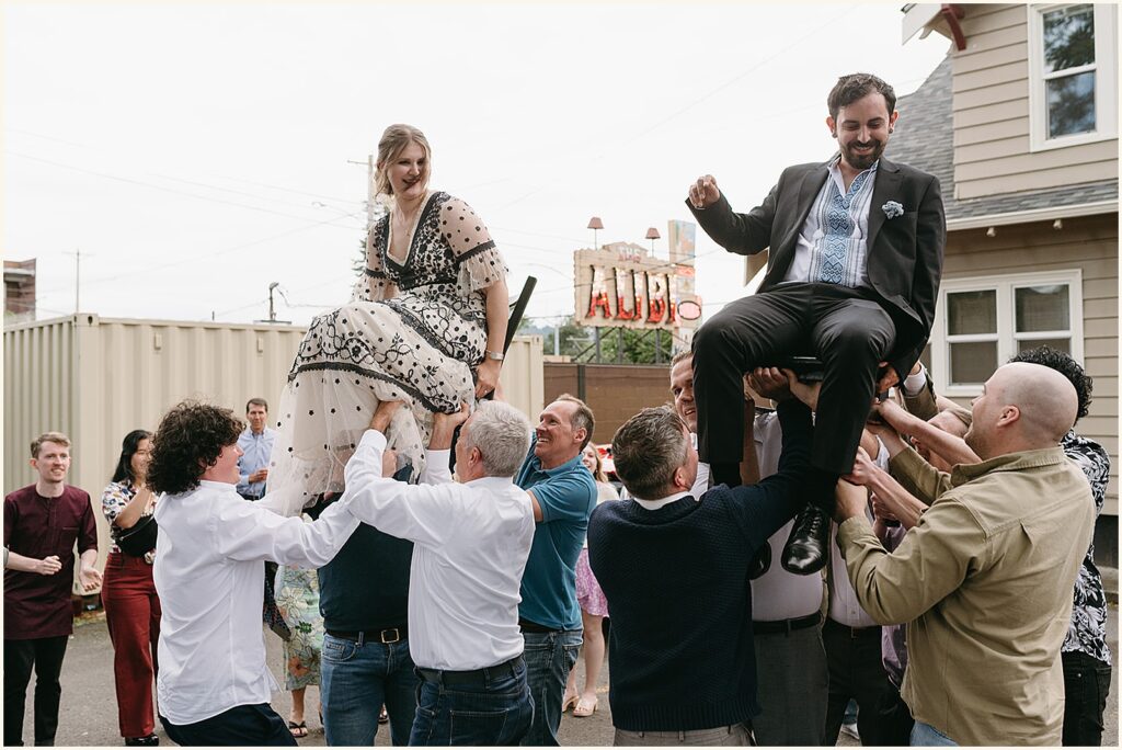 Wedding guests lift a bride and groom for the horah outside a bar at a Portland elopement.
