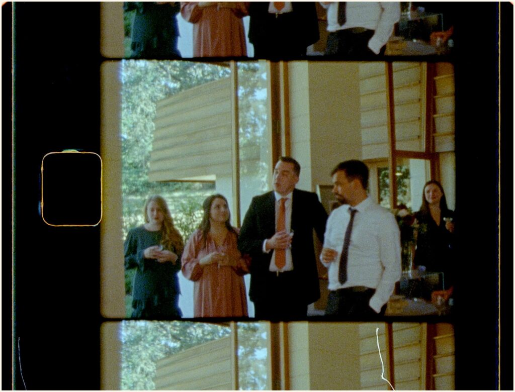 Wedding guests stand beside a window listening to a toast.