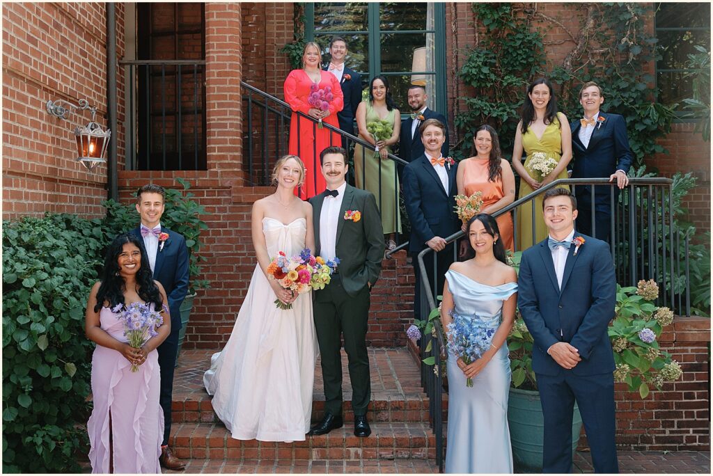 A bride and groom pose with a colorfully dressed wedding party on the steps of a Portland wedding venue.
