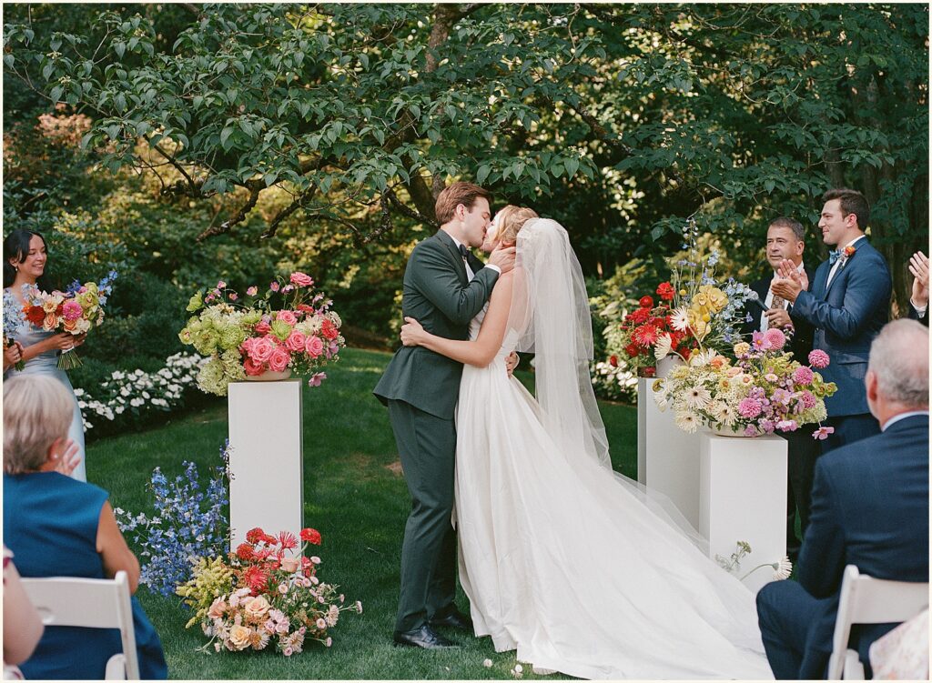 A bride and groom share a first kiss in film wedding photography.