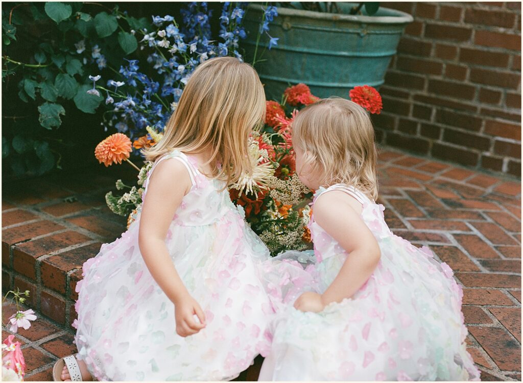 Two flower girls sit beside potted flowers in film wedding photography.